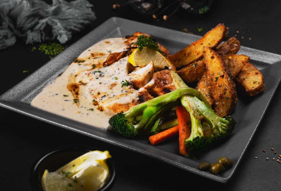 Delicious roasted chicken with sauce, vegetables, and potatoes served on a plate. Perfect for a gourmet meal.