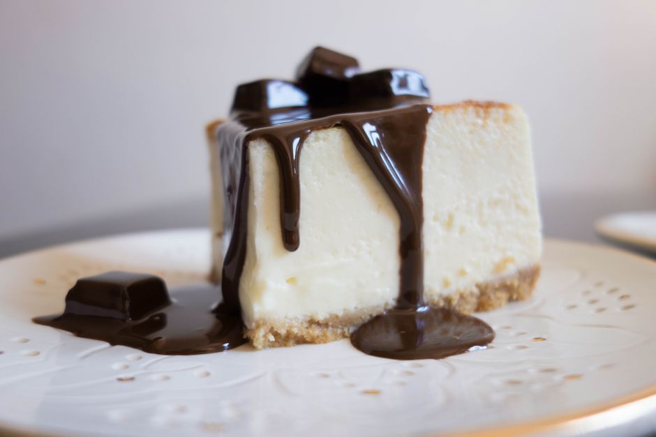 Close-up of a creamy cheesecake slice topped with rich chocolate syrup. Perfect for dessert lovers.