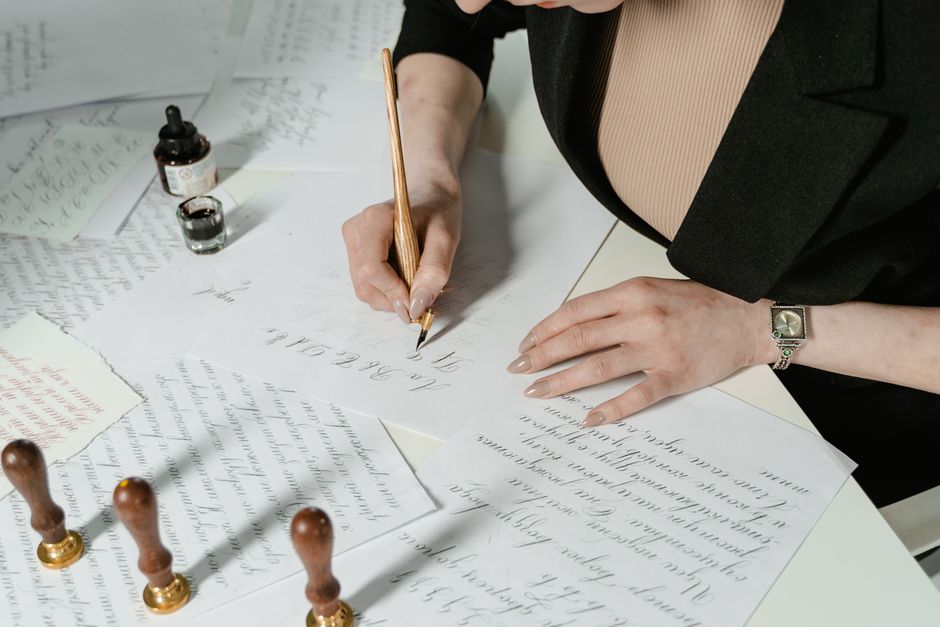 A woman practices elegant calligraphy with ink and paper, showcasing artistic hand lettering.